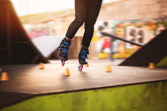 Legs on rollerblades. Orange slalom cones. Training in skatepark.