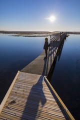 Backlit silhouette of  a man walking on a wooden pontoon over a laguna at sunset