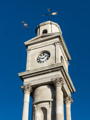 Fototapeta na wymiar The newly cleaned and refurbished Herne Bay clock tower, in Kent, Uk with a seagull flying by on a summer day with a blue sky .