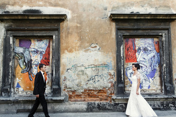 Bride and groom walk to each other before the wall with strange art
