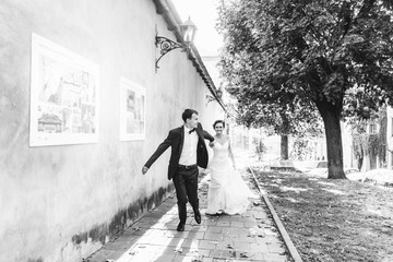 Groom holds bride's hand while they run along the street