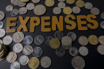 Coins on black background with word EXPENSES. Business concept