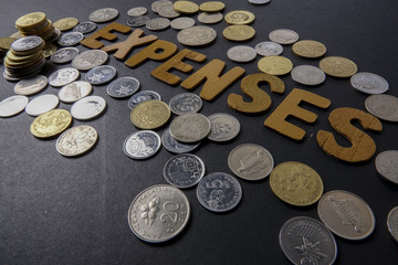 Coins on black background with word EXPENSES. Business concept