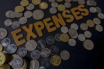 Coins on black background with word EXPENSES. Business concept