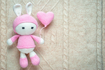 Crochet children's soft toy bunny wielding knitted balloon on the patterned knit background, with...
