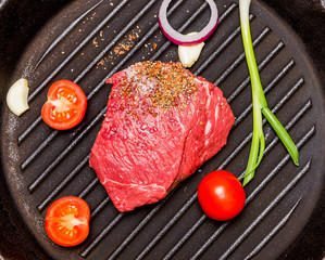 Raw beef steak with tomatoes, red and green onions, garlic, salt, lay on a cast-iron skillet.