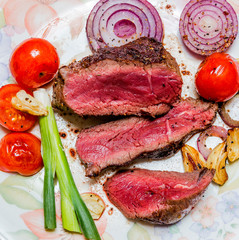 Ribeye steak with blood on a plate with tomatoes, onions, garlic, olive oil , balsamic vinegar on a wooden board.