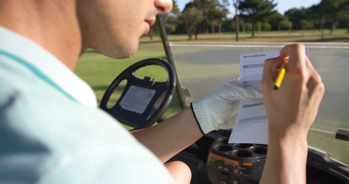 Golfer sitting in golf buggy writing on paper at golf course