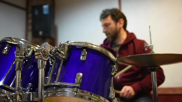 Drum set in studio, focus on toms, drummer playing instrument out of focus in background