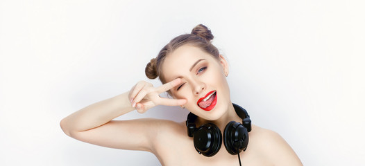 Obraz na płótnie Canvas Young pretty woman trendy makeup bright red lips bun hairstyle bare shoulders act the ape with big dj headphones on white studio background
