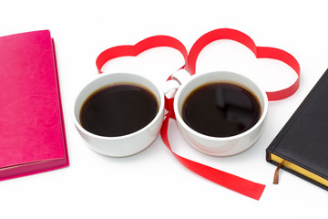 Cup of coffee, hearts of red ribbon, pink and black diaries on white background.