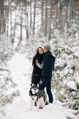 Fototapeta na wymiar Kissing couple in love and Husky dog in snowy winter forest