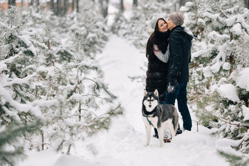 Fototapeta na wymiar Beautiful couple in love and Siberian husky dog walking in snowy pine winter forest
