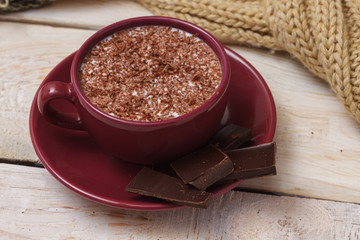 Milk chocolate in a cup on a saucer on a light wooden background