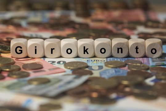 girokonto - Holzwürfel mit Buchstaben im Hintergrund mit Geld, Geldscheine