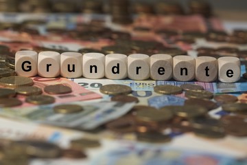 grundrente - Holzwürfel mit Buchstaben im Hintergrund mit Geld, Geldscheine