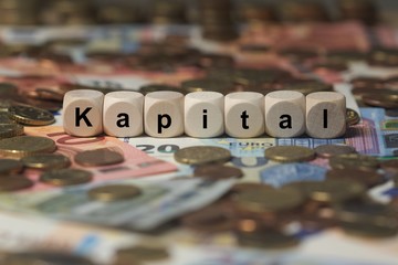 kapital - Holzwürfel mit Buchstaben im Hintergrund mit Geld, Geldscheine