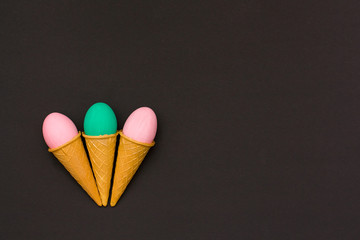 three Easter eggs in waffle cones on a black background.