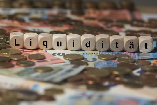 liquidität - Holzwürfel mit Buchstaben im Hintergrund mit Geld, Geldscheine