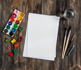 Mock up. Creative space. Artistic work tools on dark wooden table: watercolor, paintbrushes and...