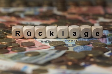 rücklage - Holzwürfel mit Buchstaben im Hintergrund mit Geld, Geldscheine