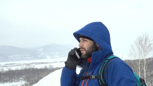 Traveler With a Beard Talking Smartphone On Mountain. Caucasian Men in Jacket looking for a GPS Signal. Mountaineer Winter Mobile Communications.Adventure Expedition Man Talk Cell Men Call Accident