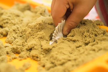 Kid's hand putting dinosaur rubber figure in the sand box