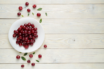 ripe cherries and leaves in a dish on a textured wooden background, view from above
