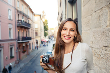 Young cheerful woman standing with camera at the balcony in european town