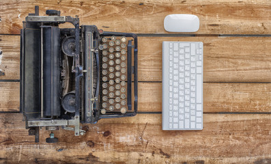 Old typewriter and a new keyboard on vintage wooden background photographed in daylight. New and old technology