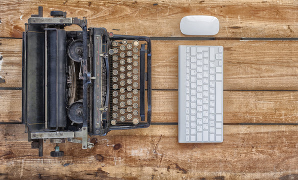 Old Typewriter And A New Keyboard On Vintage Wooden Background Photographed In Daylight. New And Old Technology