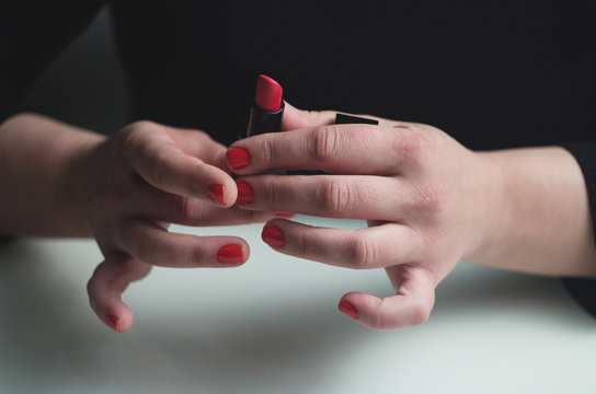 Hand with red nails holding red lipstick on the white table