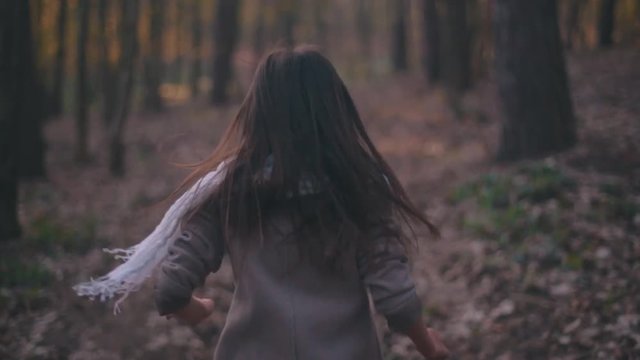 Small teenage girl with long brunette hair and stylish look. Scared little girl running in the forest, she looks around terrified as something is following her. Deserted scary forest, nightmare.