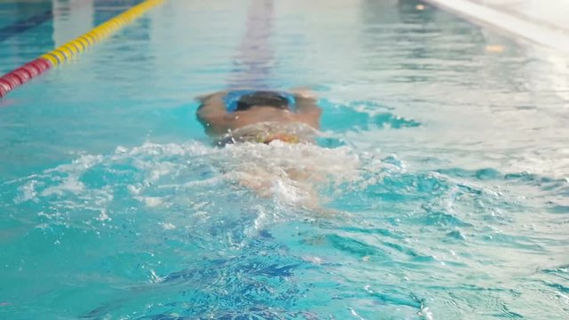 The man swims the breaststroke in the blue swimming pool