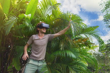 man in gray T-shirt, virtual reality 3D headset and exploring the play on a background of nature...