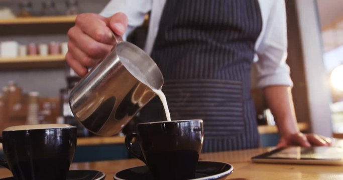 Waiter pouring milk in coffee cup while preparing coffee in cafe 4k