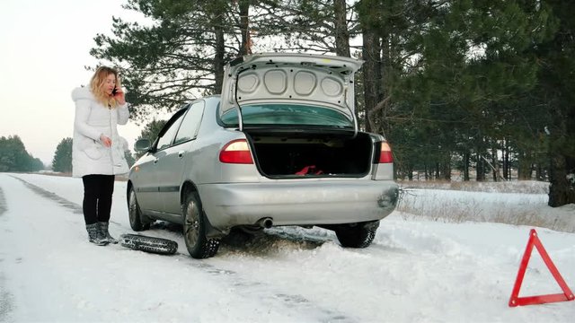reflective warning triangle before vehicle, an emergency situation on the road in winter, calls for help, woman talking on cell phone, car broke down, dangerous winter road covered with snow