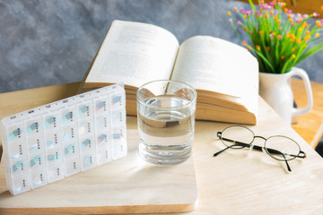 a piils of drug for weekly with water and book with glasses on t