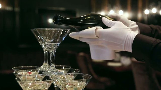 Waiter pours champagne in glass tower of champagne coctail restaurant