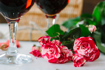 Red Valentine's day roses and glass of wine on white table