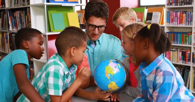 Kids and teacher looking at globe in library at elementary school 4k
