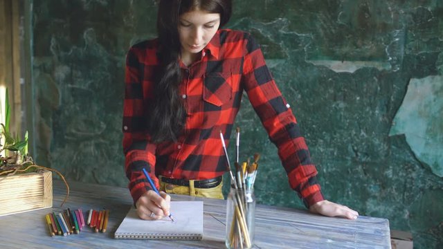 Young woman artist painting scetch on paper notebook with pencil