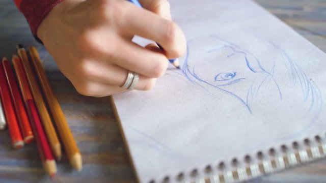 Young woman artist painting scetch on paper notebook with pencil closeup