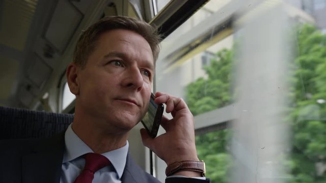 Businessman on train on his commute talking on smart phone