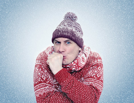 Frozen man in sweater, scarf and hat warming hands, cold, snow, blizzard