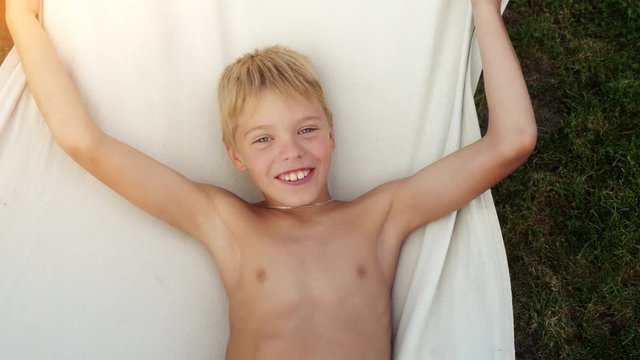 Cute happy boy relaxing in a hammock during summer vacation on beautiful warm day. Top of view. 3840x2160