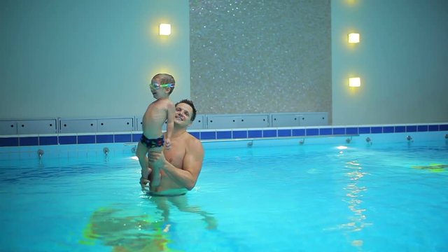The father fooling with little son in the blue swimming pool