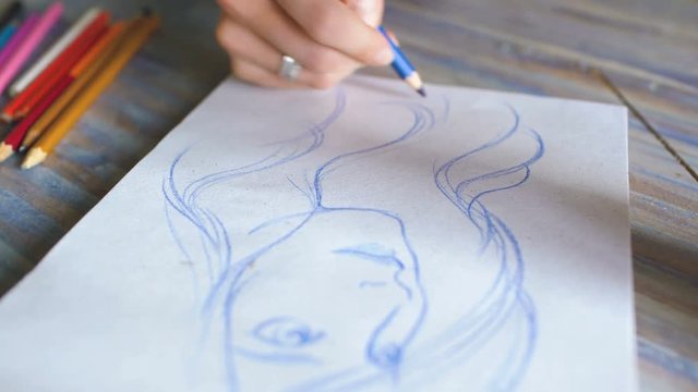 Young woman artist painting scetch on paper notebook with pencil closeup
