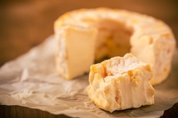 Portion cut from whole golden camembert cheese on crumpled paper sheet
