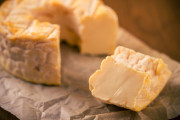 Portion cut from whole golden camembert cheese on paper sheet